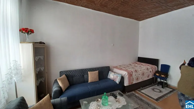 Gemütlicher Wohnbereich mit Sofa, Bett und dekorativer Deckenverkleidung, hell beleuchtet.