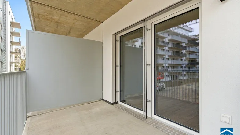 Heller Balkon mit Betonboden und Blick auf die umliegenden Gebäude der Wohnanlage.