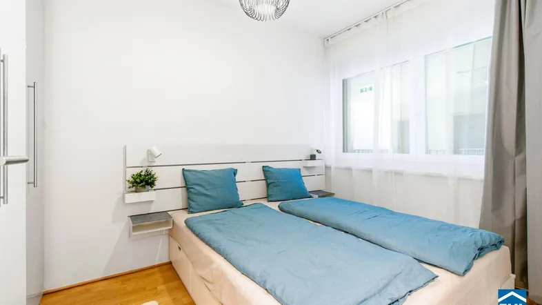Helles Schlafzimmer mit Holzboden, modernem Bett und großem Fenster für viel Tageslicht.