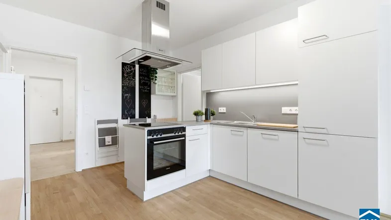 Moderne weiße Küche mit Kochinsel, integriertem Backofen und hellem Holzboden.
