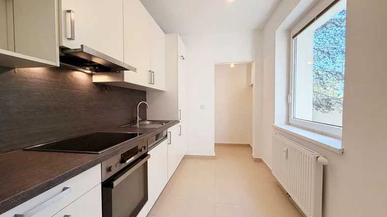 Moderne Einbauküche mit weißen Schränken, dunkler Arbeitsplatte und Fenster für natürliches Licht.