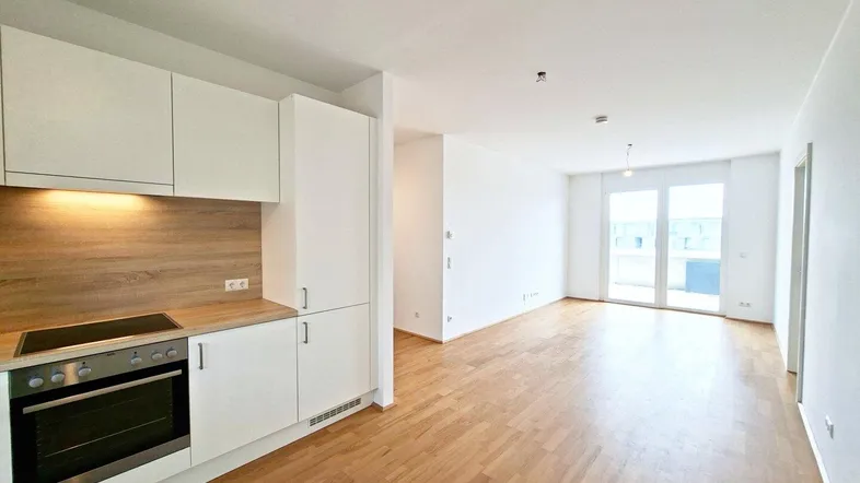 Heller offener Wohnbereich mit integrierter Küche, Parkettboden und Zugang zu einem Balkon.
