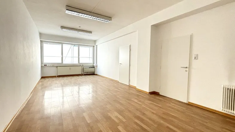 Heller, leerer Raum mit Parkettboden und großen Fenstern, ideal für flexible Nutzung.