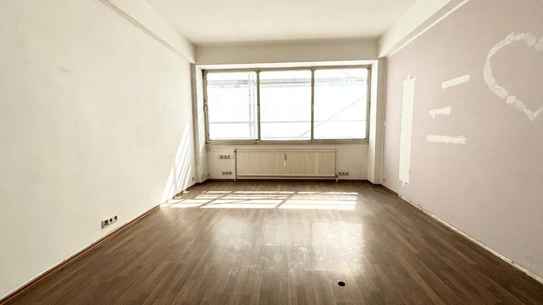 Leeres Wohnzimmer mit Parkettboden, großen Fenstern und Heizkörper unter der Fensterfront.