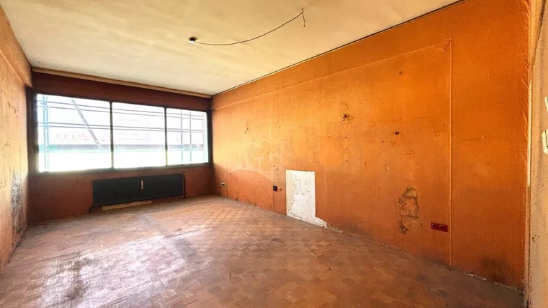 Unmöblierter Wohnraum mit orangefarbenen Wänden, Parkettboden und einem Fenster mit Heizkörper darunter.