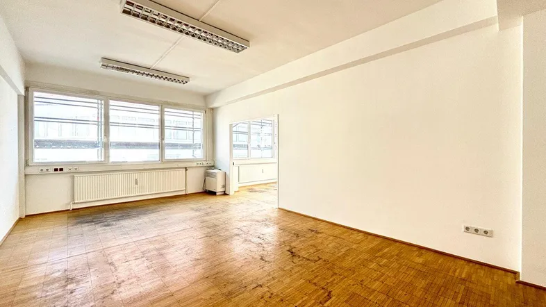 Heller, leerer Raum mit großen Fenstern und abgenutztem Holzparkettboden, bereit zur individuellen Gestaltung.