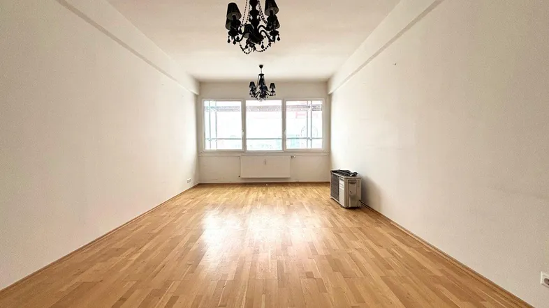 Helles, leeres Wohnzimmer mit Parkettboden, großen Fenstern und zwei schwarzen Kronleuchtern.