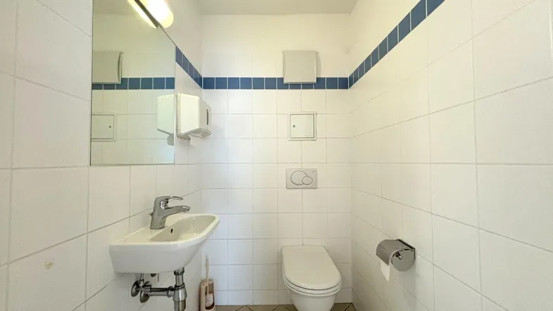 Kleines WC mit weißen Fliesen, blauem Dekorstreifen und praktischem Waschbecken.