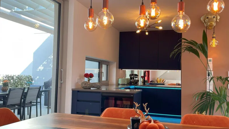 Moderner Essbereich mit Holztisch, orangefarbenen Stühlen und offener Küche, mit Zugang zur Terrasse.