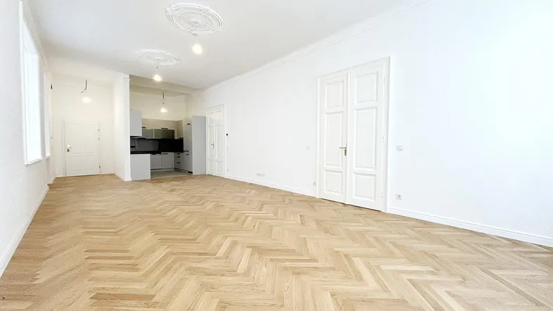 Geräumiger, heller Wohnbereich mit Fischgrätparkett, hohen Decken und Stuckelementen, offen zur Küche.