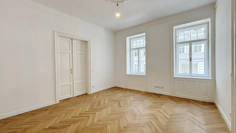 Helles Zimmer mit Fischgrätparkett, hohen Decken und Stuckverzierung, ideal als Wohn- oder Schlafzimmer.