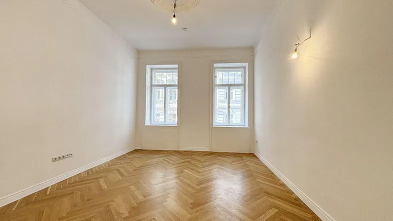 Helles Zimmer mit Fischgrätparkett und Stuckdecke, ideal als Wohn- oder Schlafzimmer.