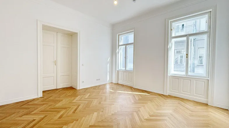 Helles Zimmer mit Fischgrätparkett, hohen Decken und Stuckverzierung, ideal als Wohn- oder Schlafzimmer.