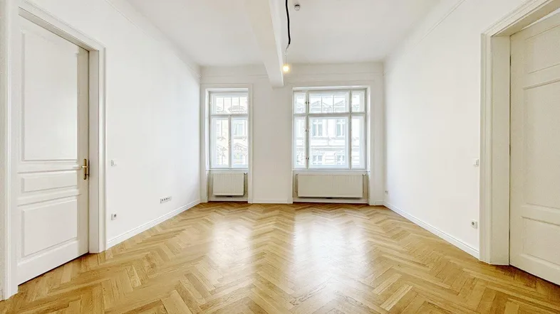 Helles Zimmer mit Fischgrätparkett und hohen Fenstern, ideal als Wohn- oder Schlafzimmer nutzbar.