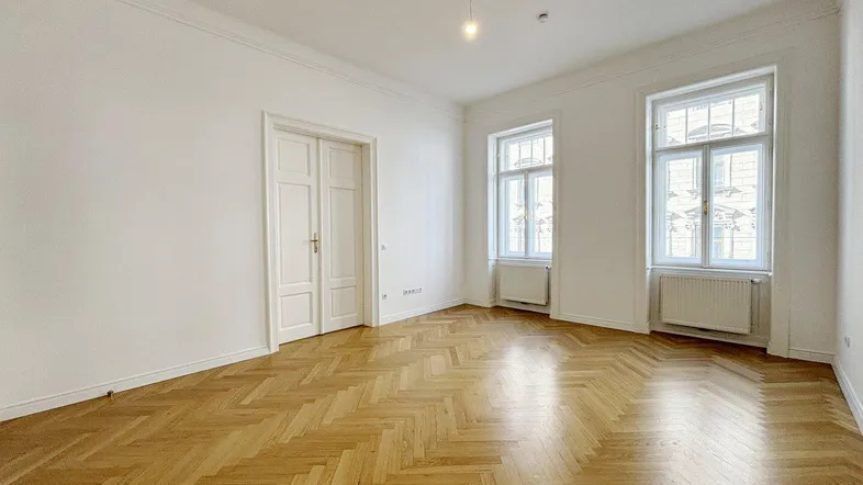 Helles Zimmer mit Fischgrätparkett, hohen Decken und Stuckelementen, ideal als Wohn- oder Schlafzimmer.