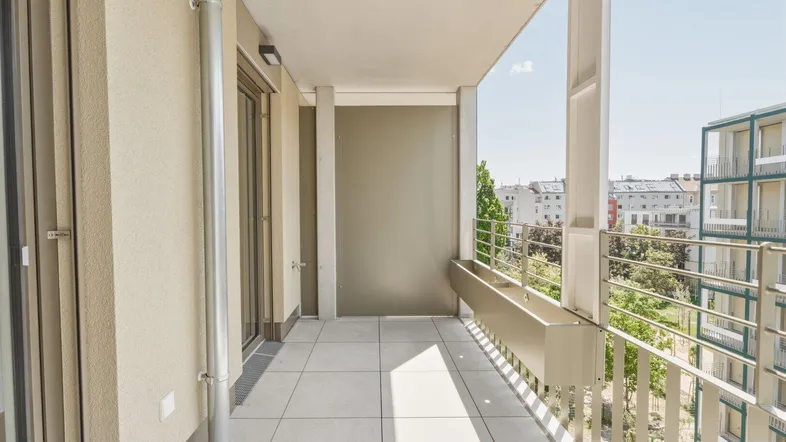 Heller Balkon mit Fliesenboden und Metallgeländer, bietet einen Ausblick auf die umliegenden Gebäude und Bäume.