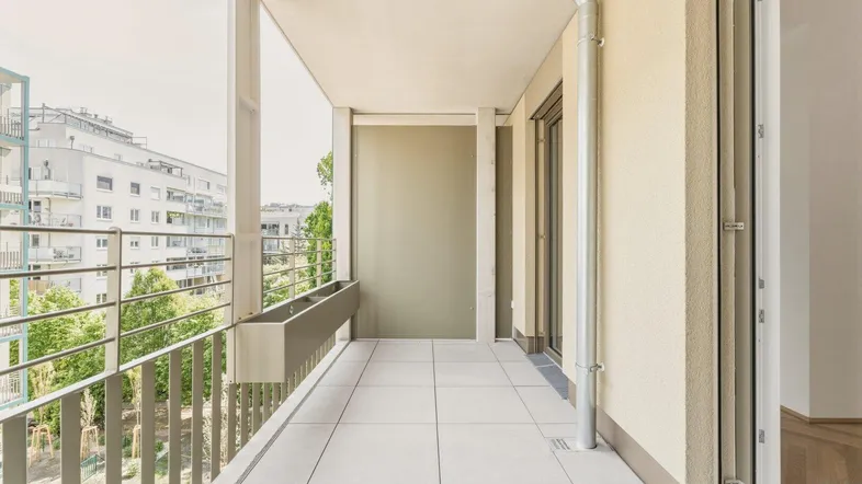 Heller Balkon mit Fliesenboden und Blick auf die umliegenden Gebäude und grüne Bäume.