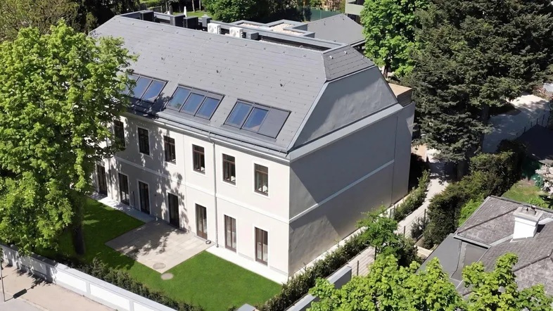 Luftaufnahme eines modernen Neubaus mit Satteldach, Dachfenstern und gepflegtem Gartenbereich.