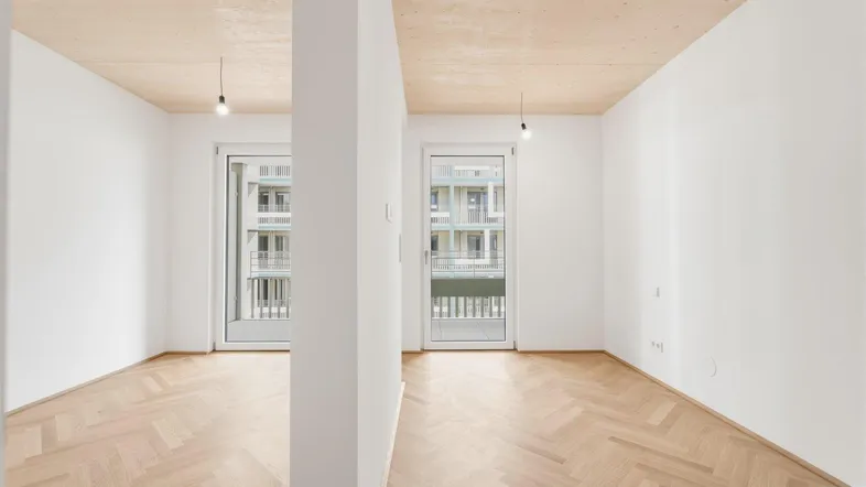 Heller, leerer Raum mit Fischgrätparkett und Zugang zu einem französischen Balkon, bereit zur Einrichtung.