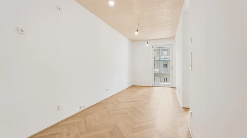 Helles, leeres Zimmer mit Fischgrätparkett und Holzbalkendecke, bereit zur individuellen Gestaltung.