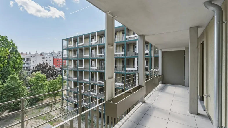 Langer Balkon mit Fliesenboden und Blick auf die umliegenden Gebäude und Grünflächen.