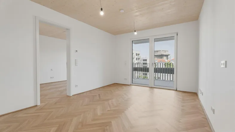 Helles Zimmer mit Fischgrätparkett, Holzbalkendecke und Zugang zu einem Balkon.