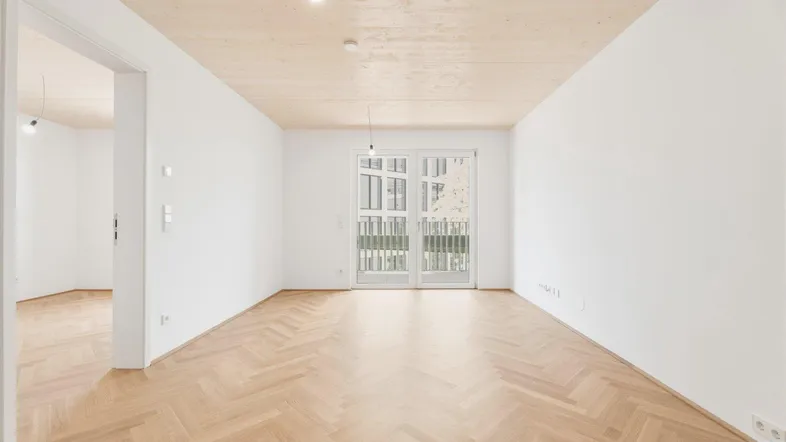 Helles Zimmer mit Fischgrätparkett, Holzbalkendecke und Zugang zu einem französischen Balkon.