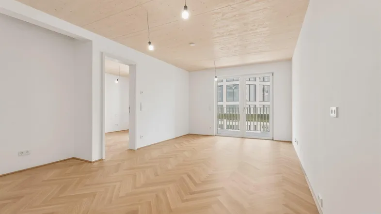 Helles Zimmer mit Fischgrätparkett und Holzbalkendecke, bereit zur individuellen Gestaltung.