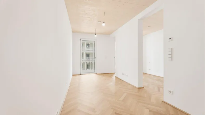 Helles, unmöbliertes Zimmer mit Fischgrätparkett und Zugang zu einem französischen Balkon.
