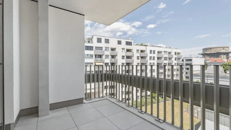 Geräumiger Balkon mit Fliesenboden und Blick auf umliegende Wohngebäude unter blauem Himmel.