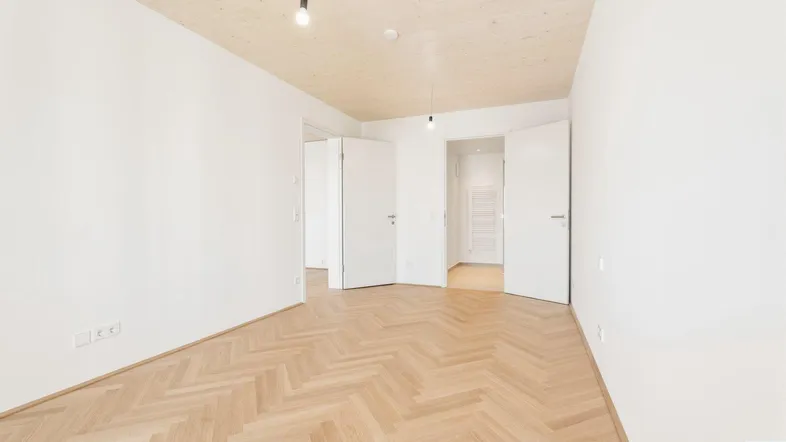 Heller Raum mit Fischgrätparkettboden, weißen Wänden und einer Holzdecke, der vielseitig nutzbar ist.