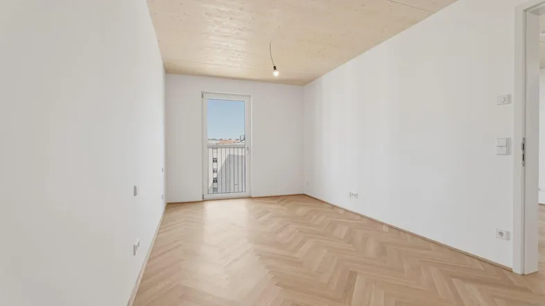 Helles Zimmer mit Fischgrätparkett, Holzbalkendecke und Zugang zu einem französischen Balkon.