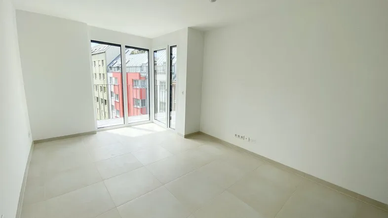 Helles Zimmer mit großen Fenstern, Fliesenboden und Zugang zu einem Balkon mit Stadtblick.