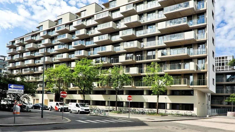 Modernes Wohngebäude mit vielen Balkonen und großen Fenstern in städtischer Umgebung.