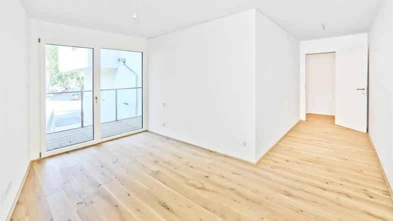 Helles Zimmer mit Holzboden und Zugang zu einem Balkon, ideal als Wohn- oder Schlafbereich.