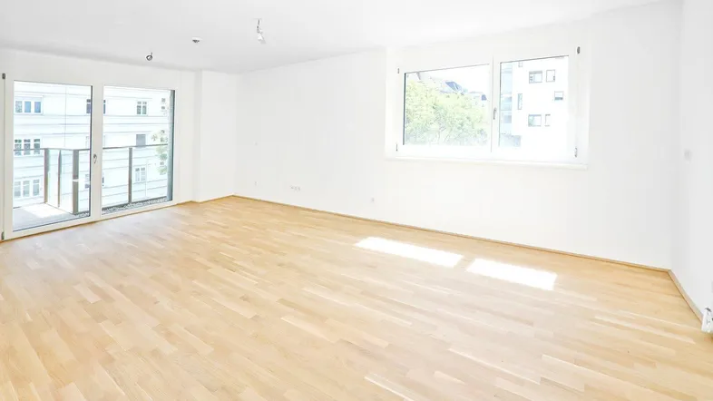Helles, leeres Zimmer mit Holzboden und Zugang zu einem Balkon, ideal für Wohn- oder Schlafbereich.