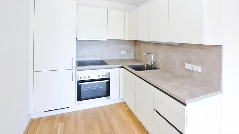 Moderne Einbauküche mit weißen Hochglanzfronten, hellen Arbeitsplatten und Holzboden.