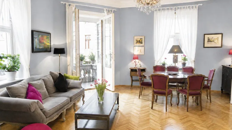 Heller Wohn- und Essbereich mit Fischgrätparkett, Kronleuchter und Zugang zu einem charmanten Balkon.