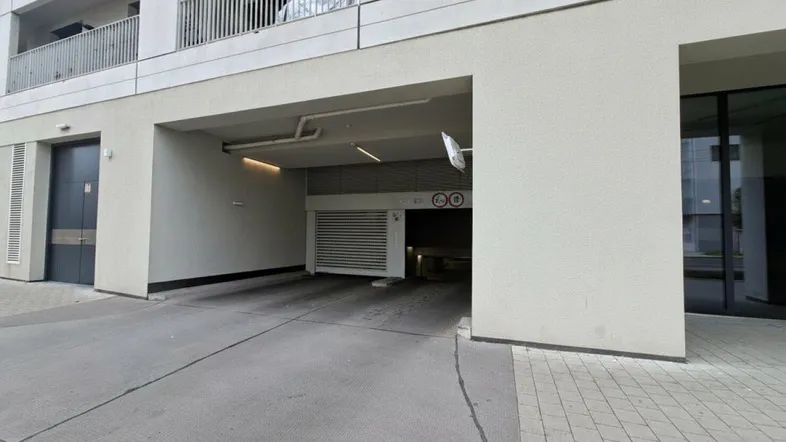 Einfahrt zur Tiefgarage eines modernen Wohngebäudes mit klaren Linien und Balkonen im Hintergrund.