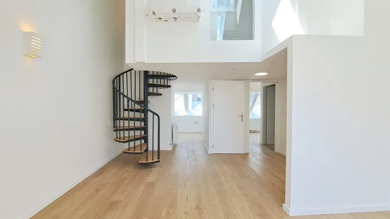 Heller Wohnbereich mit Holzparkettboden, Wendeltreppe und hohen Decken, die viel Tageslicht hereinlassen.