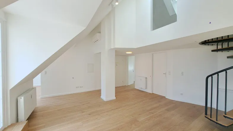 Heller, offener Wohnbereich mit hohen Decken, Holzfußboden und einer eleganten Wendeltreppe zum Obergeschoss.