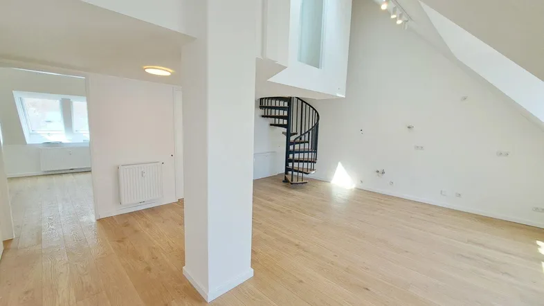 Helles Dachgeschoss-Wohnzimmer mit Holzparkettboden, Wendeltreppe und schrägen Decken.