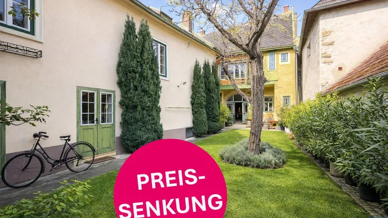 Gepflegter Gartenbereich mit Rasenfläche und altem Baumbestand vor einem traditionellen Gebäude.