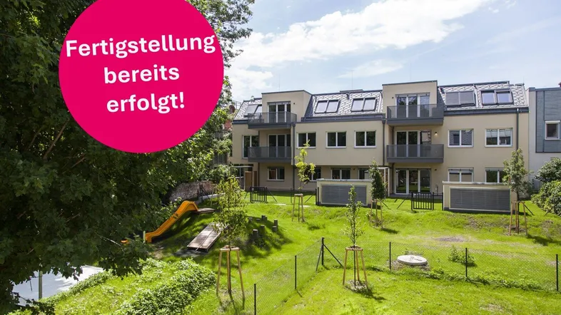 Modernes Mehrfamilienhaus mit Balkonen, gepflegtem Garten und Kinderspielplatz unter blauem Himmel.