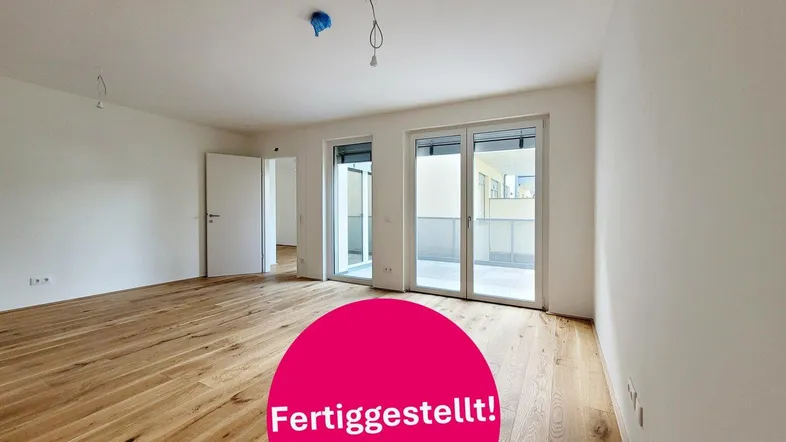 Heller, unmöblierter Raum mit hochwertigem Holzboden und großen Fenstern zum Balkon.