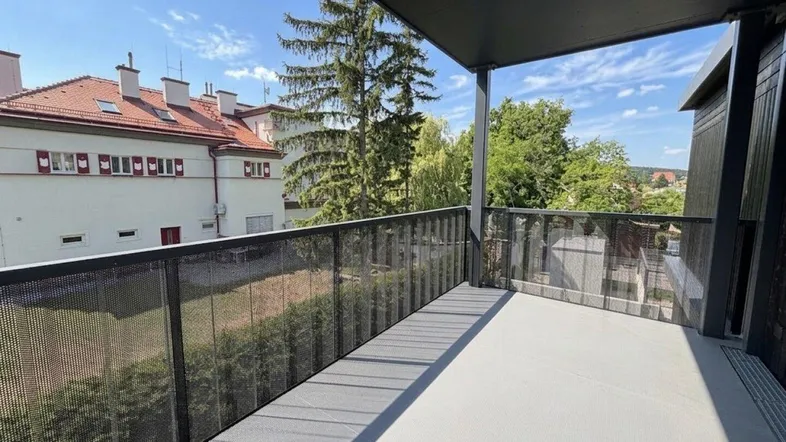 Geräumiger Balkon mit modernem Metallgeländer und Blick auf grüne Bäume und Nachbargebäude.
