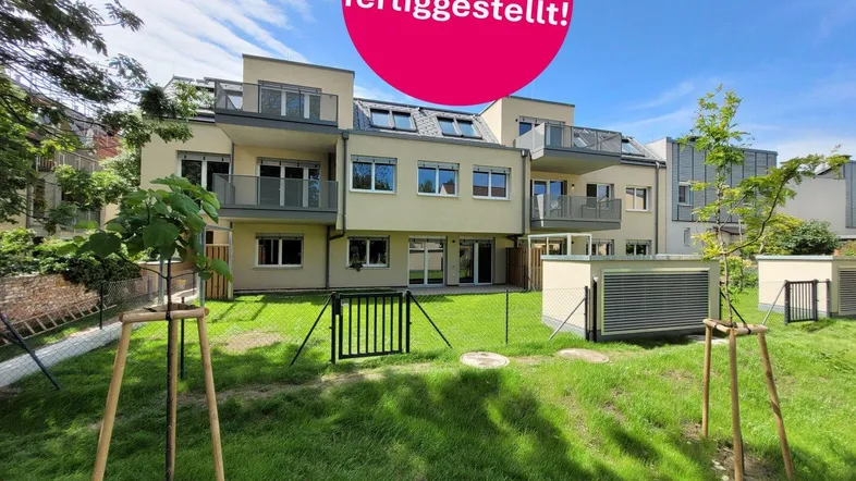 Modernes Mehrfamilienhaus mit Balkonen und großzügiger Grünfläche im Vordergrund, kürzlich fertiggestellt.