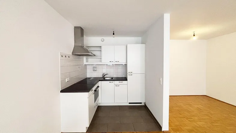 Moderne Küchenzeile mit weißen Schränken und dunkler Arbeitsplatte, offen zum Wohnbereich.