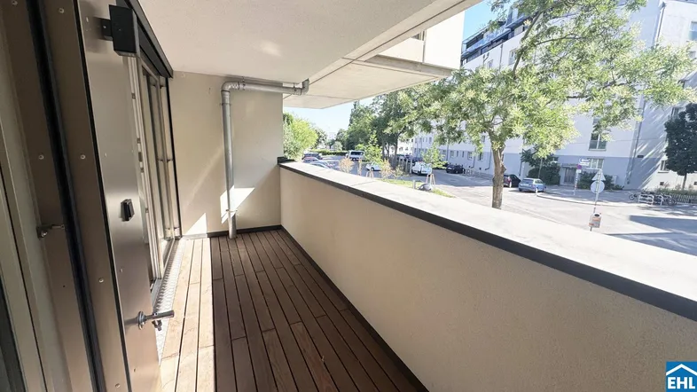 Heller Balkon mit Holzboden und Blick auf die Straße sowie umliegende Gebäude.