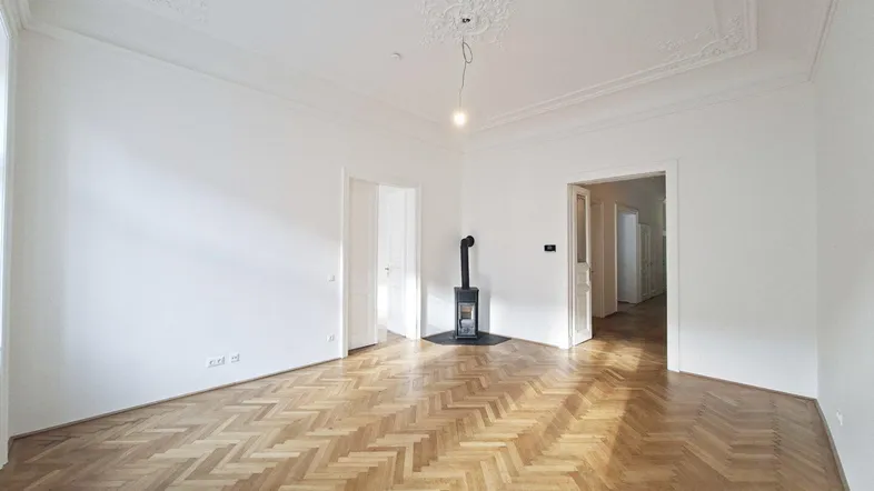 Helles Wohnzimmer mit Fischgrätparkett, Stuckdecke und modernem Kaminofen.
